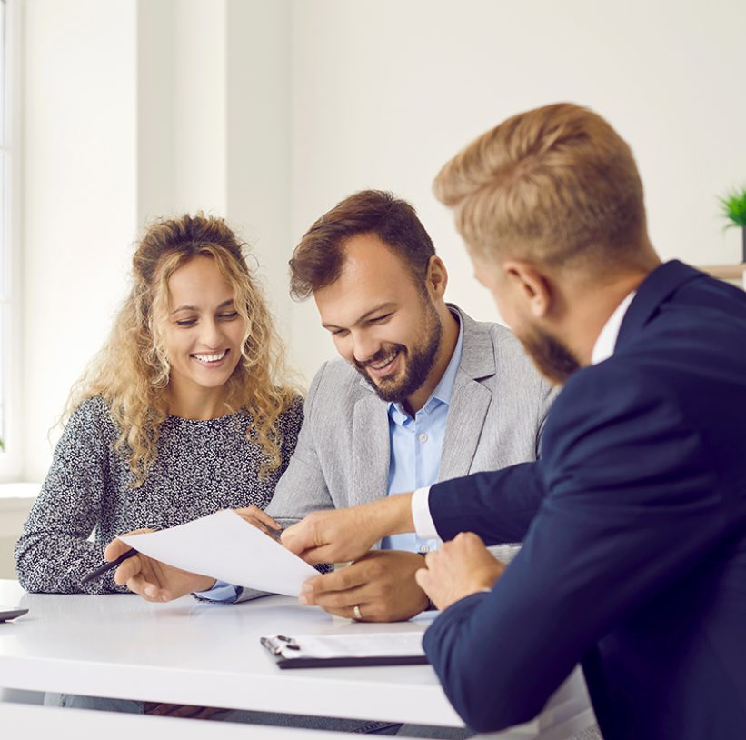 Happy young family at meeting in office signs document on purchase of real estate or loan agreement. Head of bank, realtor or financial advisor submits contract and indicates place of its signing..