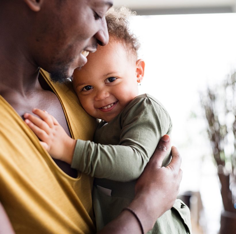 Close up of young afro-american father at home with his cute little daughter holding her in the arms.