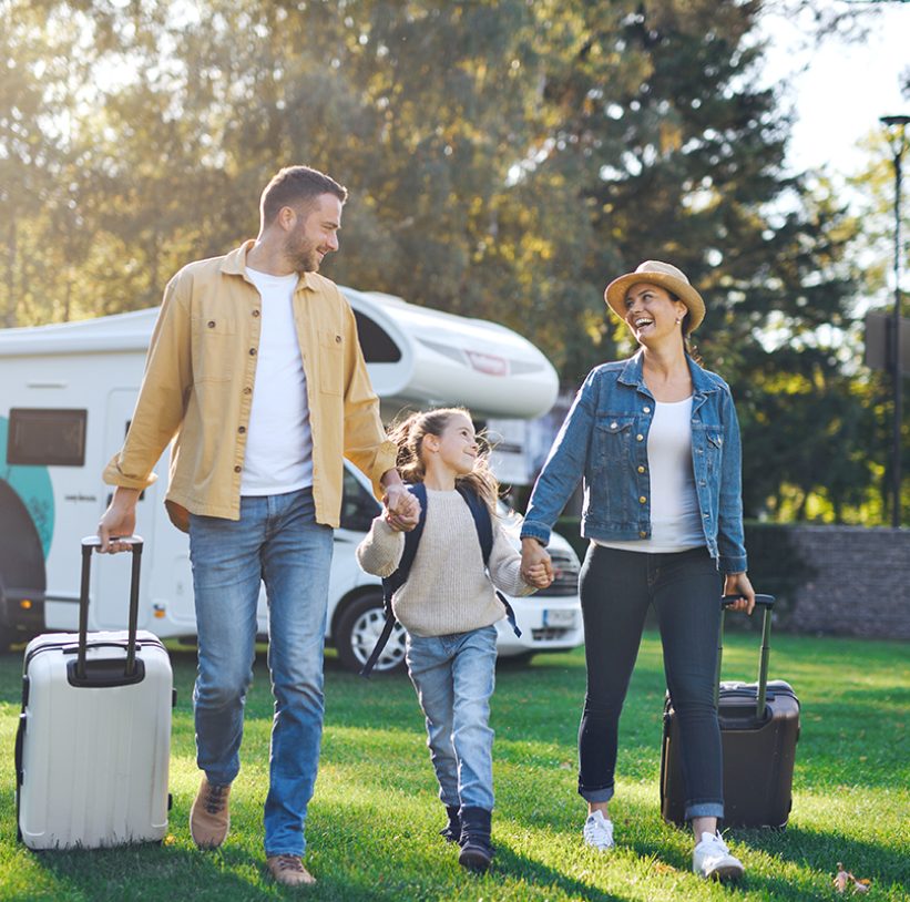 A happy young family walking with suitcases, coming home from caravan trip outdoors in garden